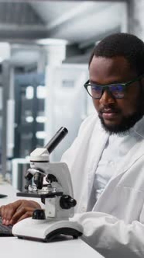 Man in Lab Coat Adjusts Microscope in Laboratory
