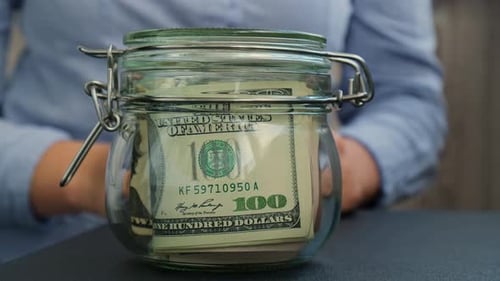 Female Hands Turn Glass Jar Full of American Currency Dollars Cash Banknote with Text 2026 Year