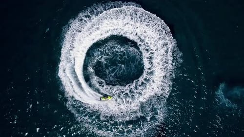 Aerial view of 2 people driving a jet ski creating a perfect spiral in the deep blue waters of Cypru