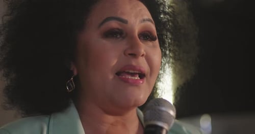 Side view of a woman holding a microphone, delivering an inspiring speech