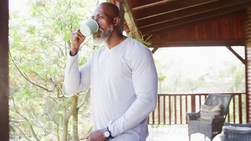 Man Drinking Coffee on Cabin Porch in Nature