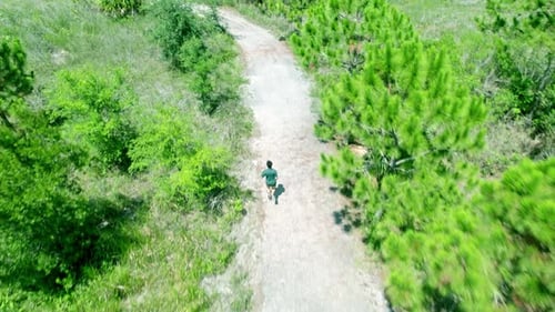 Aerial follow drone shot. Video from above of a man wearing green t shirt running along a country r