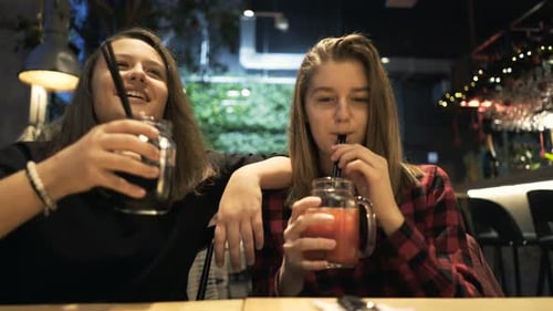Cheerful teenage girlfriends enjoying fresh drinks and happy conversation in a cafe