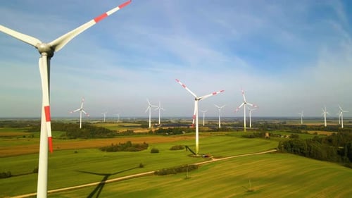 Drone shot of the wind turbines working in a wind farm generating green electric energy on a wide gr