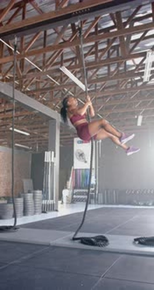 Vertical video: Climbing rope in gym, woman in athletic wear exercising upper body strength