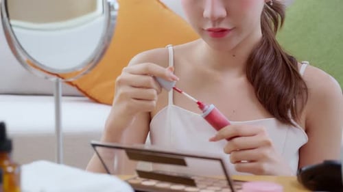 Closeup hand beauty young asian woman applying makeup with lipstick looking mirror in living room.