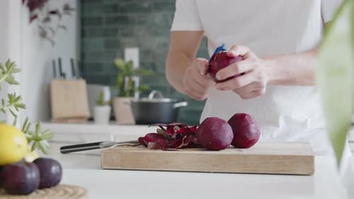 Medium shot of a man peeling fresh beetroot with a peeler in a modern kitchen