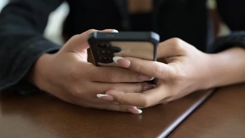 Close-up of woman hands texting and chatting using mobile phone indoors during day in coffee shop
