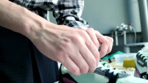 Jovem amarra tênis elegantes na mesa da oficina