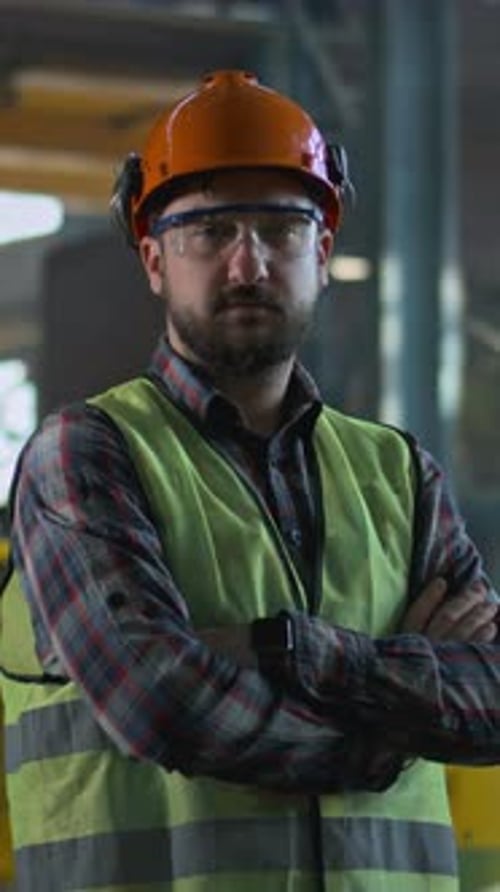 Heavy Industry Worker Stands at Manufacturing Facility and Looks at Camera