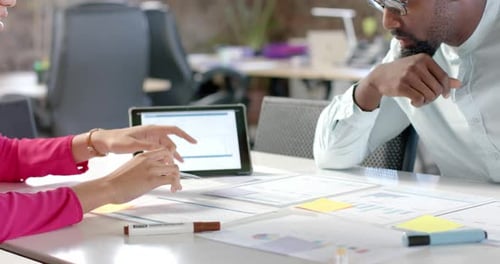 Diverse colleagues discussing work with documents on table and tablet in office in slow motion