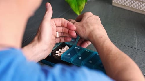 Un homme trie ses pilules et ses suppléments dans un organiseur de pilules hebdomadaire Concept de gestion des médicaments