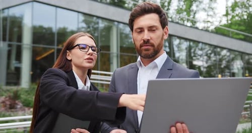 Closeup of Businessman and Businesswoman Standing Outdoors Reviewing Important Information on Laptop