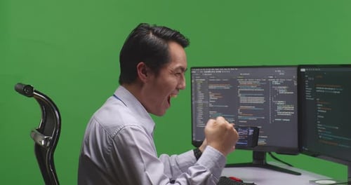 Developer Looking At Code On Mobile Phone While Write Code With Multiple Screens In Green Screen