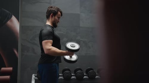 Weightlifting athlete do standing dumbbell biceps curls at indoor gym