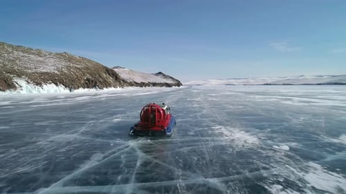 Aerial View on the Hovercraft Driving on Cracked Snowy Ice of Baikal Along the Rocky Cliff Drone