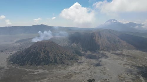 Aerial view of active volcano with crater in depth. Brown dirt around. clouds of smoke on volcano