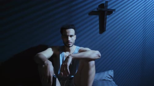 Pensive Young Man Sitting at Night with Cross