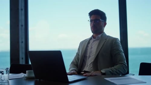 Serious Businessman Using Laptop Computer in Sea View Office. Focused Professional Typing