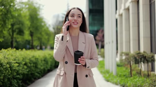 Woman Discussing Plans on Phone Call and Enjoying Coffee While Walking in Park