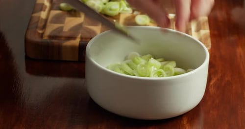 Closeup of a Chef's Hands Transferring Chopped Fresh Green Onions Coarsely Sliced Into Rings From a