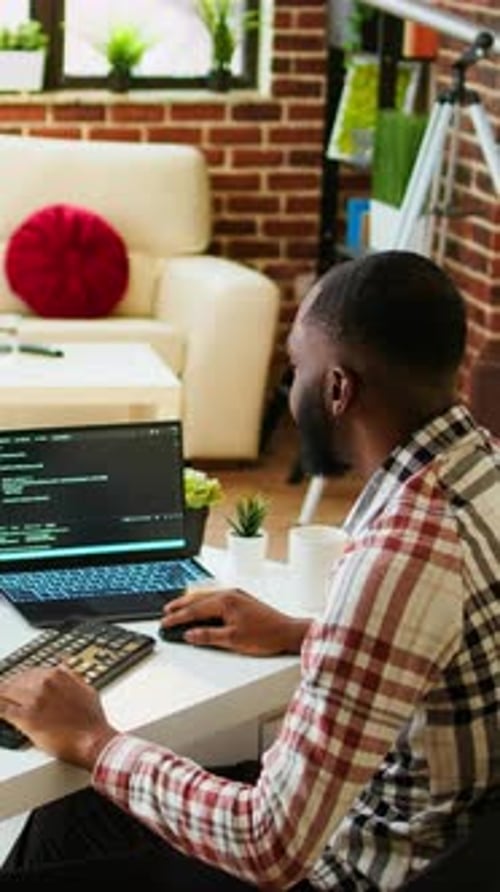 Vertical Video Young Man Seen Programming Software Code on His Laptop in a Sleek Home Office