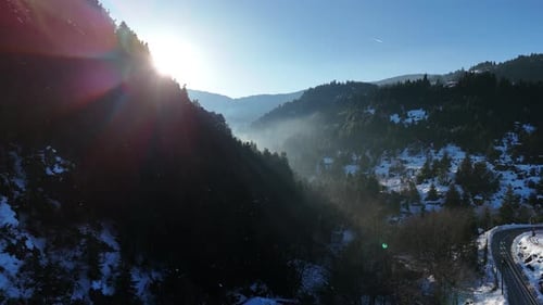 Prise de vue
cinématographique par drone des montagnes enneigées du centre de la Grèce. Rayons du soleil à travers la forêt avec un éclat de lentille.