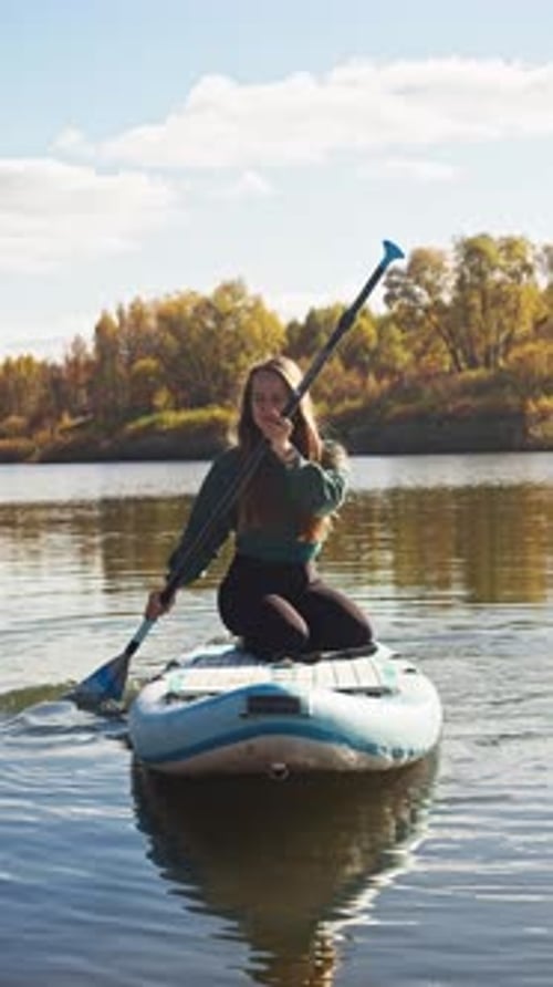 A Beautiful Young Woman with Blonde Hair is Rafting on a River Using an Inflatable Surfboard