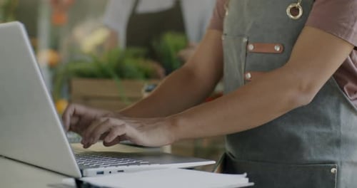Closeup of Female Hands Working with Computer at Flower Shop Counter While Saleswoman Caring for