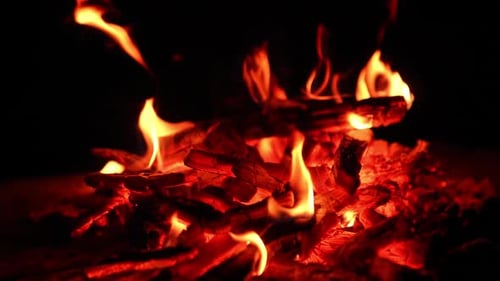 Pieces of smoldering burnt out wooden logs in the campfire.