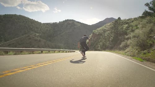 One skateboarder guy bombing a steep hill in Colorado backcountry on a skateboard