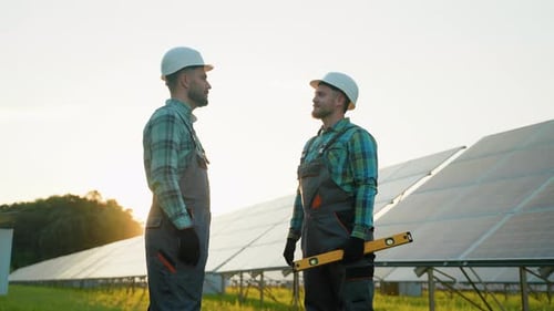 Two Engineers Shaking Hands at a Solar Panel Farm During Sunset
