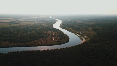 Luftaufnahme der Flussbiegung, die durch ein Tal zwischen Wiesen und Wäldern fließt, mit leichtem Dunst
