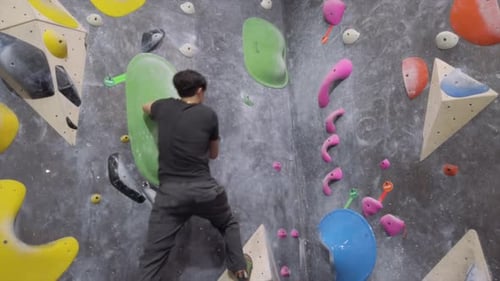 Asian climber guy climbing up outdoor bouldering wall at fitness gym