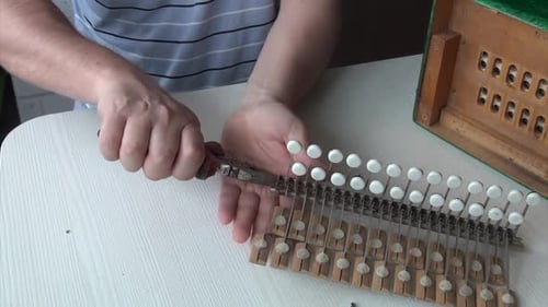 Person Repairing an Old Wooden Accordion with Pliers