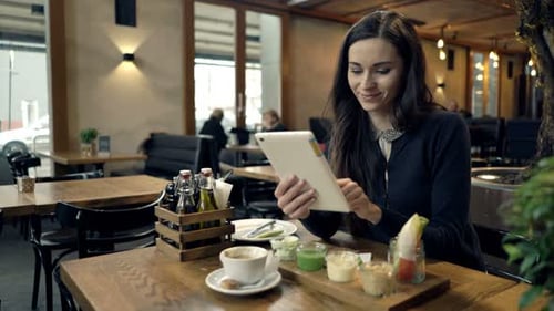 Young, Happy Woman Using Tablet Computer During Meal in Cafe 30s