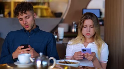 Portrait of Caucasian Male and Female Sitting in Restaurant and Texting on Smartphones