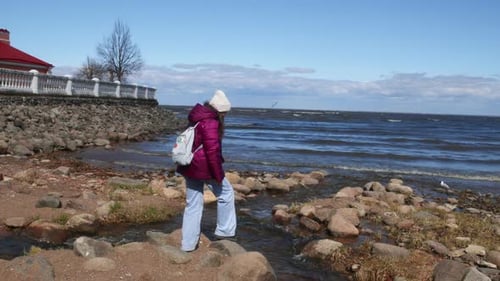 Woman Tourist Backpacker Standing on Stones on Sea Shore in Windy Weather