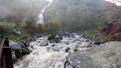Zeitlupe, felsiger, fließender Wasserfall, Flusswasser, das auf eine neblige Felsformation am Flussufer spritzt
