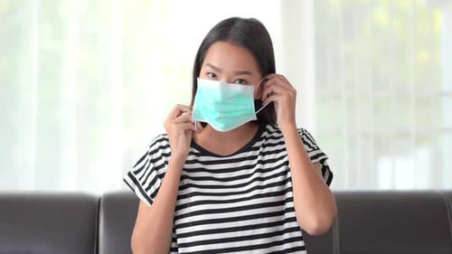 A very attractive young woman demonstrates putting her surgical mask on.