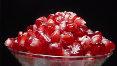 Red pomegranate seeds in a cup. Rotating on a black background, close-up.