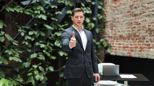 Confident Businessman in Suit Gives Thumbs Up in Modern Office