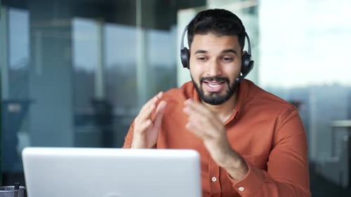 Man talking on headset using laptop at office