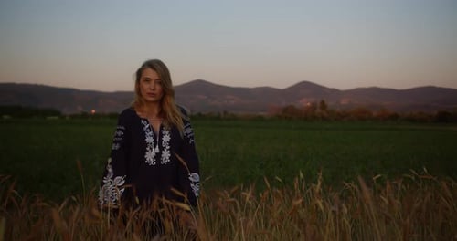 Young romantic woman in national clothes on a field of wheat at sunset or sunrise