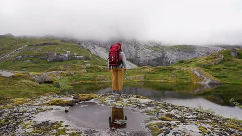 Traveler with a Big Red Backpack Stopped Near the Lake Enjoys the View of the Foggy Tops of the