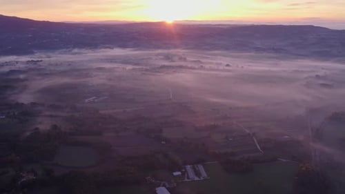 Aerial view of foggy sunrise over fields and valley, Italy.