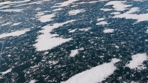 Gros plan d'un lac gelé percé d'un trou dans la glace, entouré de motifs de givre. L'obscurité