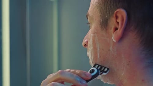 Man Shaves Face in Modern Bathroom
