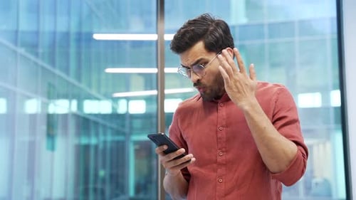 Confused Man Looking at Cell Phone Inside Office