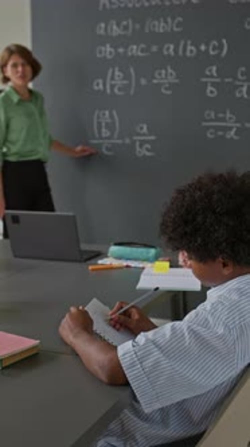 Student Raises Hand in Classroom with Teacher Presenting